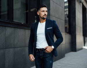 Guter Style für Männer hier als Mann in Jeans mit weißem Hemd und offenem Sakko, trägt eine Uhr an der Hand, die er locker in die Hosentasche steckt